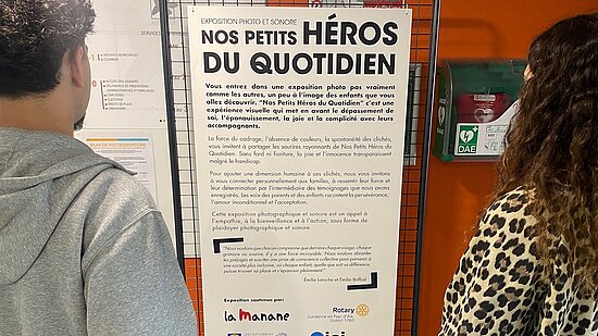 Deux persoones lisent une affiche intitulée nos petits heros du quodidien